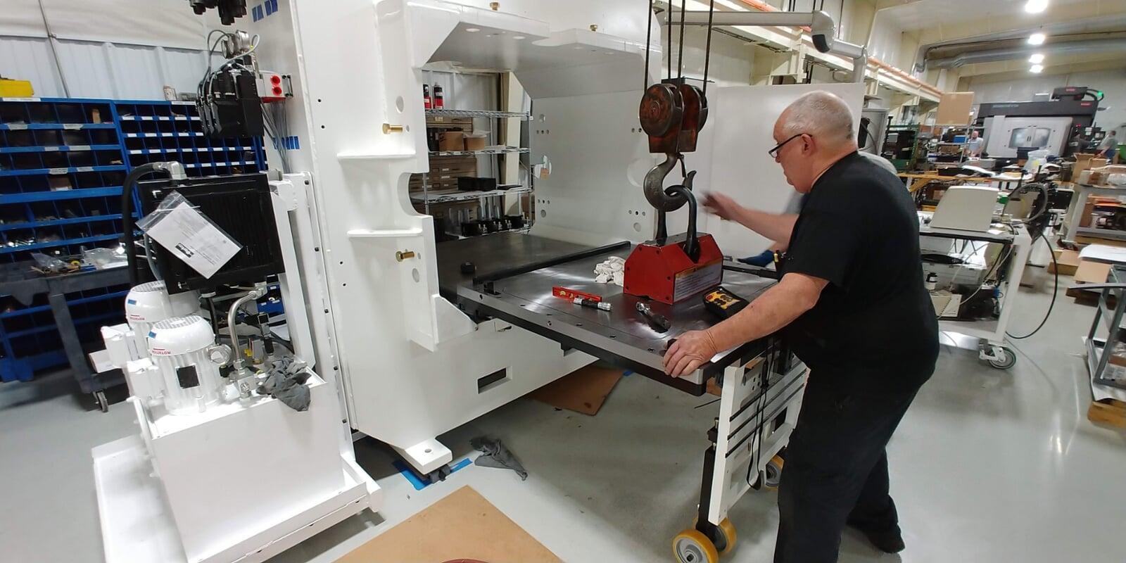 A mechanic carefully installs a press platten using a lifting magnet and overhead crane. This step was enabled by careful design for assembly in the engineering phase